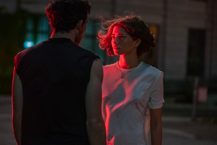 Zendaya as Tahsi Duncan standing in a white shirt with a bob lit by red car lights opposite Josh O'Connor as Patrick in Challengers.
