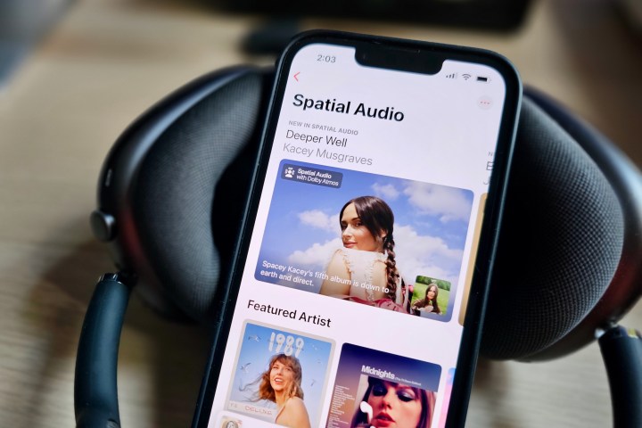 Apple AirPods Max kulaklık setinin yanında, Spatial Audio içeriğiyle ilgili bir özellik sayfasının yer aldığı Apple Music uygulamasını gösteren bir Apple iPhone 14.