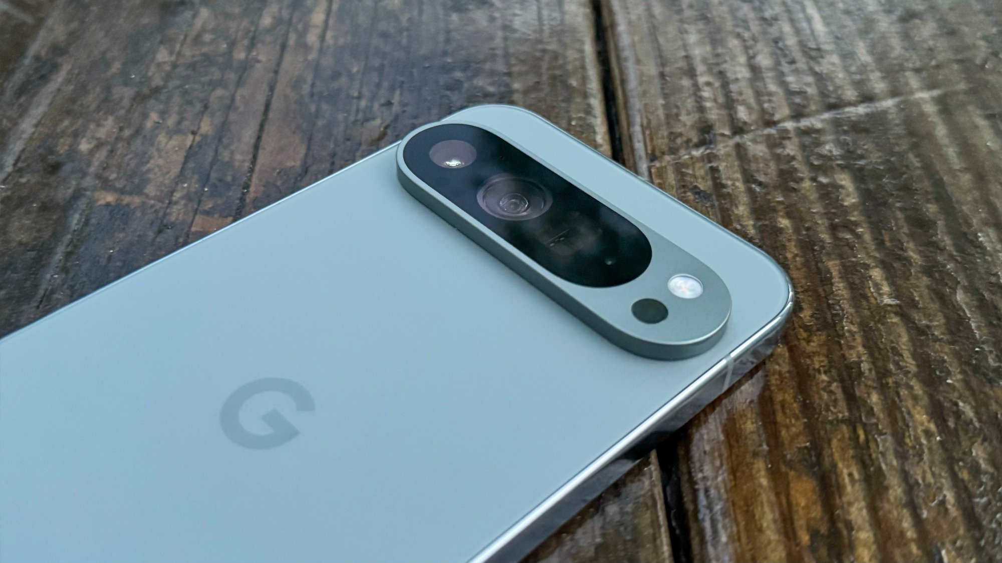 Ahşap bir yüzey üzerinde Google Pixel 9 Pro XL'ın yakın çekimi, ekranı aşağı bakacak şekilde ve arka kamera görülebilecek şekilde.